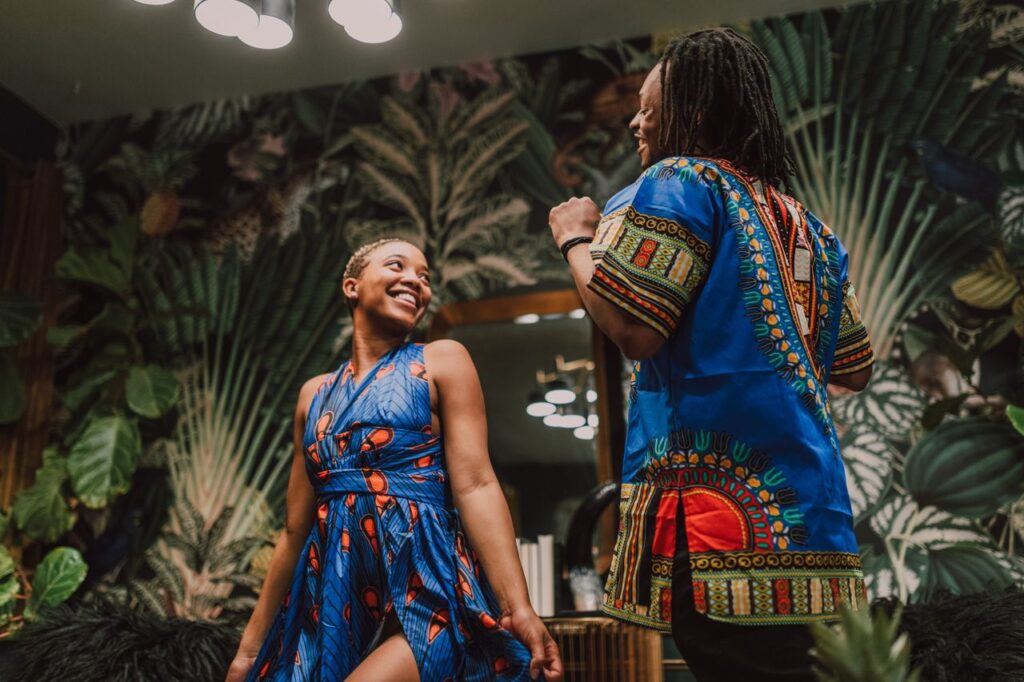 Happy couple celebrating in colorful African attire, embracing culture and tradition indoors.